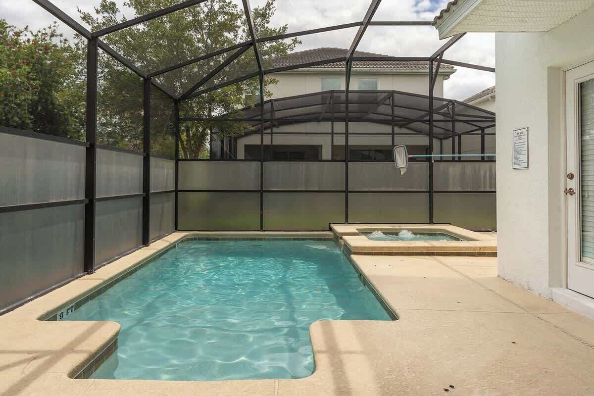 Una piscina rectangular con cerramiento de vidrio, un jacuzzi y un área de terraza techada.