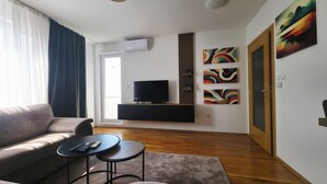Een moderne woonkamer met een bank, een televisie op een zwart dressoir, twee bijzettafels en een deur.