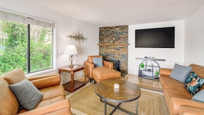 A modern living room with leather sofas, a round coffee table, a fireplace, and a large flat-screen TV mounted on the wall. - Walk to Beaches: Waterfront Home in Port Orchard! (Port Orchard)