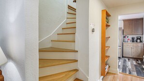 A staircase with wooden steps leading to a landing, a kitchen area with wooden cabinets and a refrigerator, and a small shelf with a plant. - Walk to Beaches: Waterfront Home in Port Orchard! (Port Orchard)