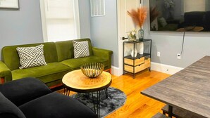 Een woonkamer met een groene bank, een ronde houten salontafel en een zwarte fauteuil.