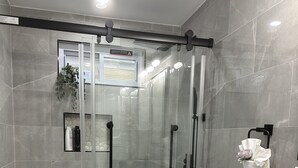 Een moderne badkamer met een glazen douchecabine, een badkuip, een toilet en een wastafelmeubel met een wastafel.