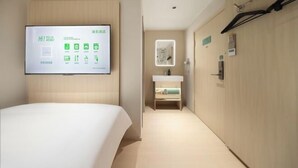 A hotel room with a bed, a wall-mounted TV displaying room information, a bathroom with a sink and mirror, and a hallway with a coat rack. - Hi Inn (Beijing Tiananmen National Grand Theater) (Beijing)