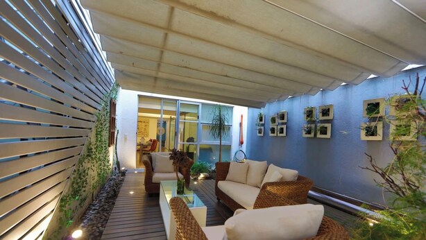Un espace de détente extérieur moderne, avec des meubles en osier, une table basse en verre et un chemin bordé de plantes.