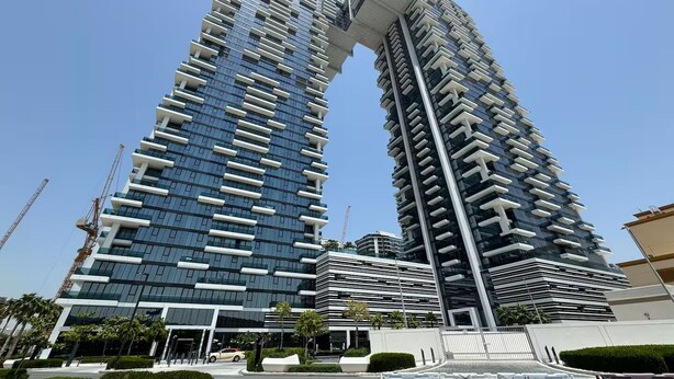A modern high-rise building with a unique architectural design, featuring a series of balconies and a prominent overhanging structure at the top. - Vogue| Al Wasl 1 Residence near World Trade Centre (Dubai)