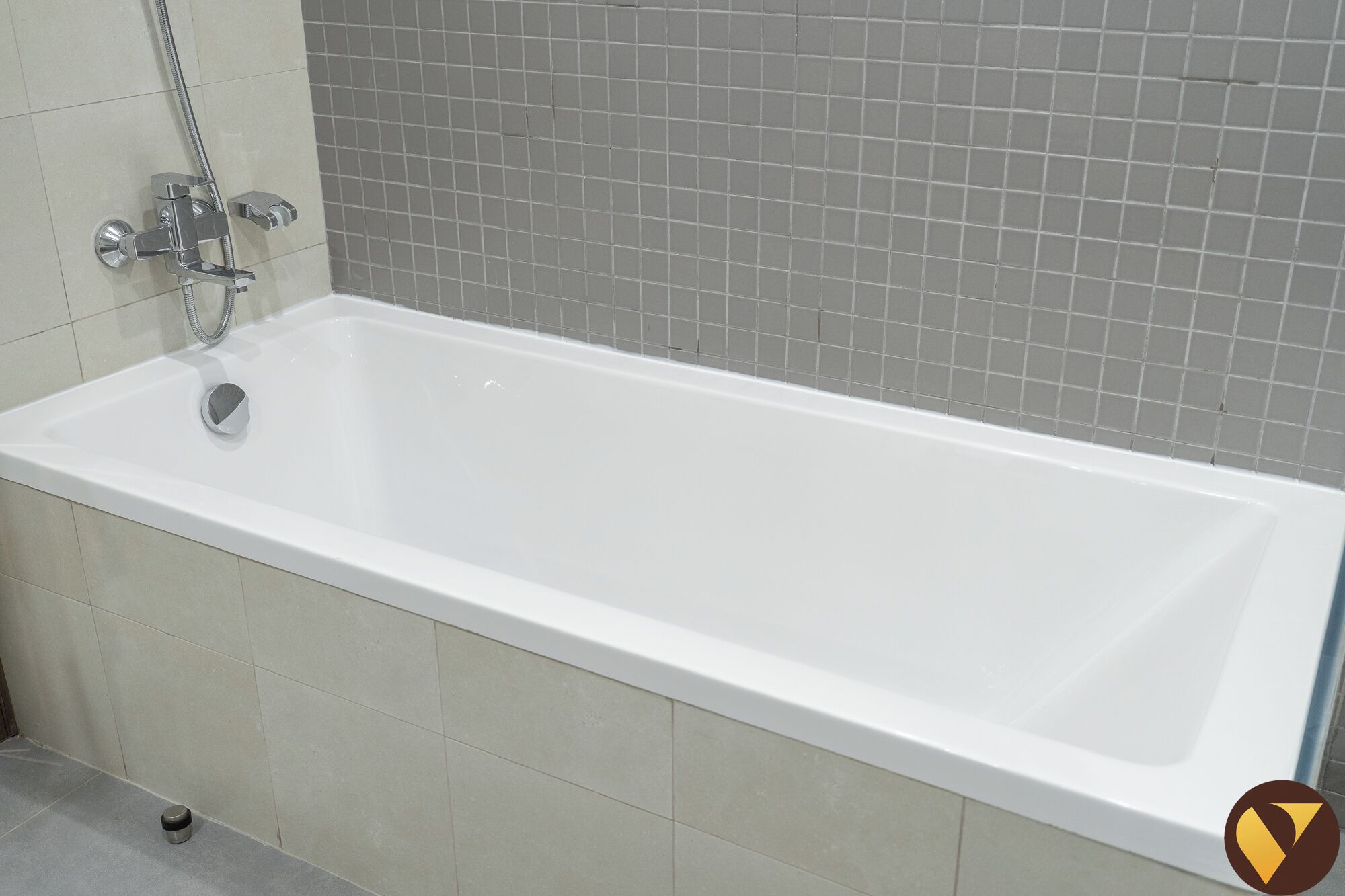 A standard rectangular bathtub with a chrome faucet and shower head, set against a tiled wall.