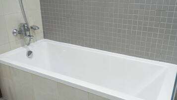 A standard rectangular bathtub with a chrome faucet and shower head, set against a tiled wall.