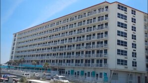 Un hotel de varios pisos con balcones, estacionamiento al frente y mesas de picnic.