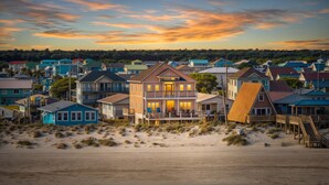 A beachfront property with a prominent house featuring a balcony and multiple windows, surrounded by other houses and a sandy beach. - Surf City Shores / Ocean Views, Hot Tub & Beach Access (Surf City)