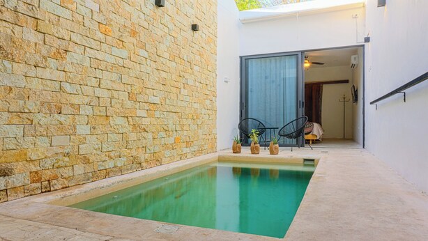 Ein moderner Poolbereich mit einer Steinmauer, einem kleinen Pool und einer Tür zu einem Raum mit einem Bett und einem Sessel.