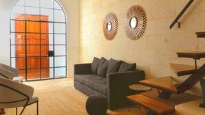 Ein modernes Wohnzimmer mit grauem Sofa, Couchtisch aus Holz und einem großen Fenster mit Blick auf eine Holztür.