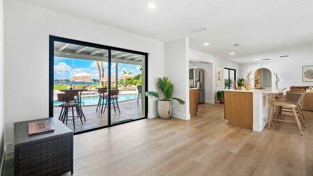A spacious living area with a large sliding glass door leading to a poolside area, a kitchen with a central island, and a seating area with a view of the outdoors. - The Garden of Eden | Beautiful Villa w/ Pool & Game Room (West Palm Beach)