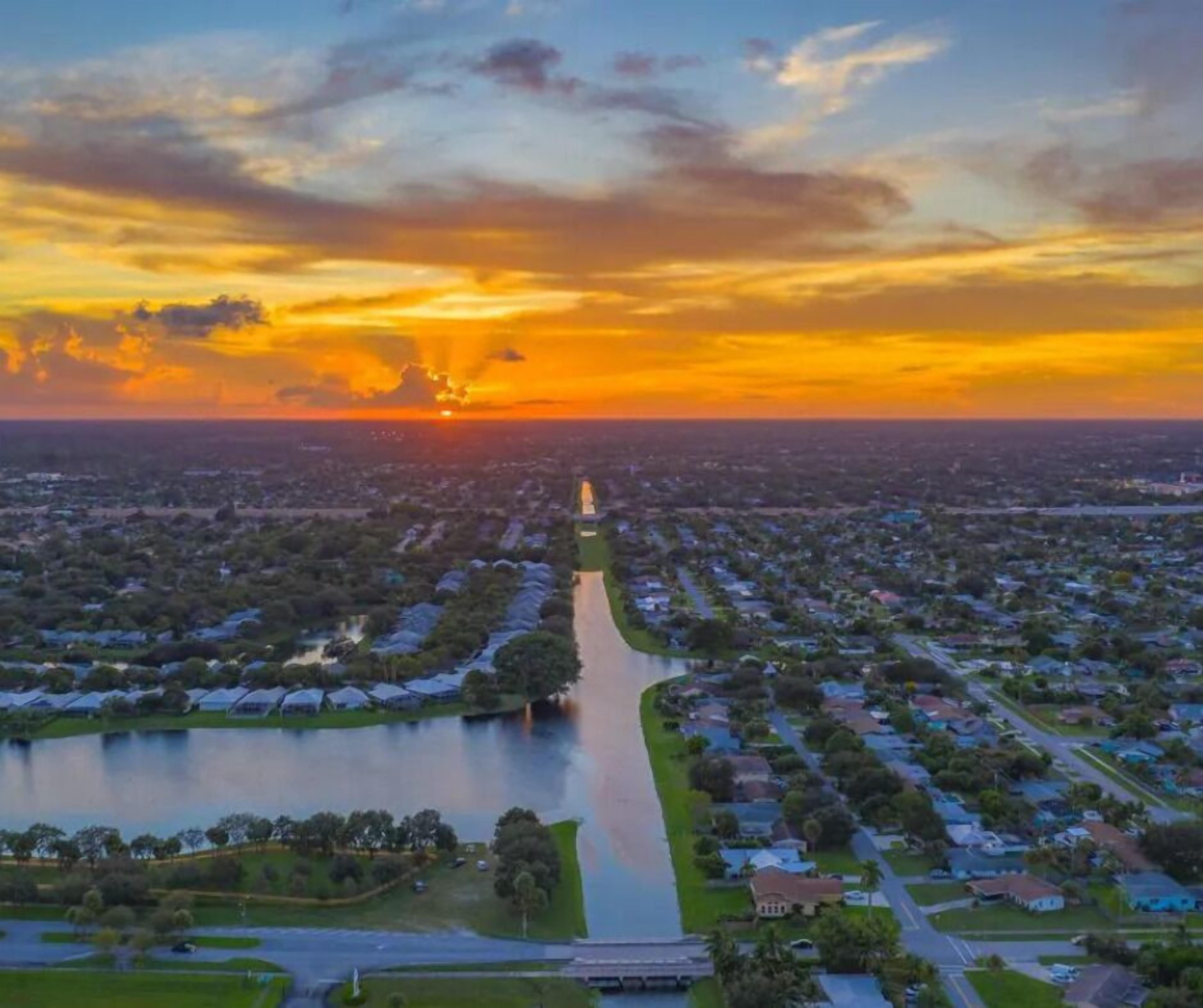An aerial view of a residential area with houses, a river, and a bridge during sunset.