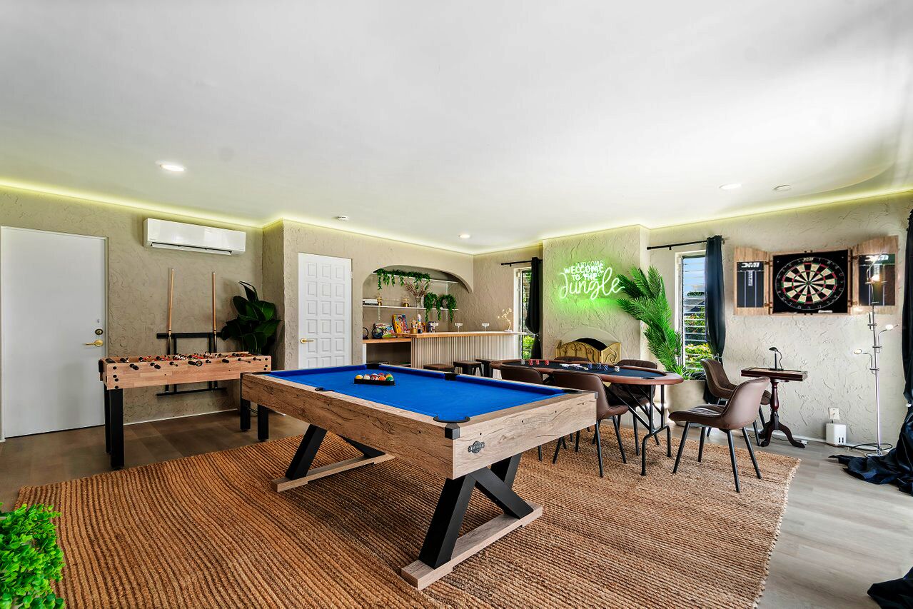 Un espace de loisirs intérieur moderne, équipé d’une table de billard, d’un baby-foot et de cibles de fléchettes.