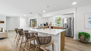 A modern kitchen with a central island, stainless steel appliances, and a seating area with wicker chairs. - The Garden of Eden | Beautiful Villa w/ Pool & Game Room (West Palm Beach)