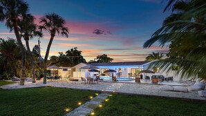 A resort with a pool, outdoor seating, and palm trees. - The Garden of Eden | Beautiful Villa w/ Pool & Game Room (West Palm Beach)