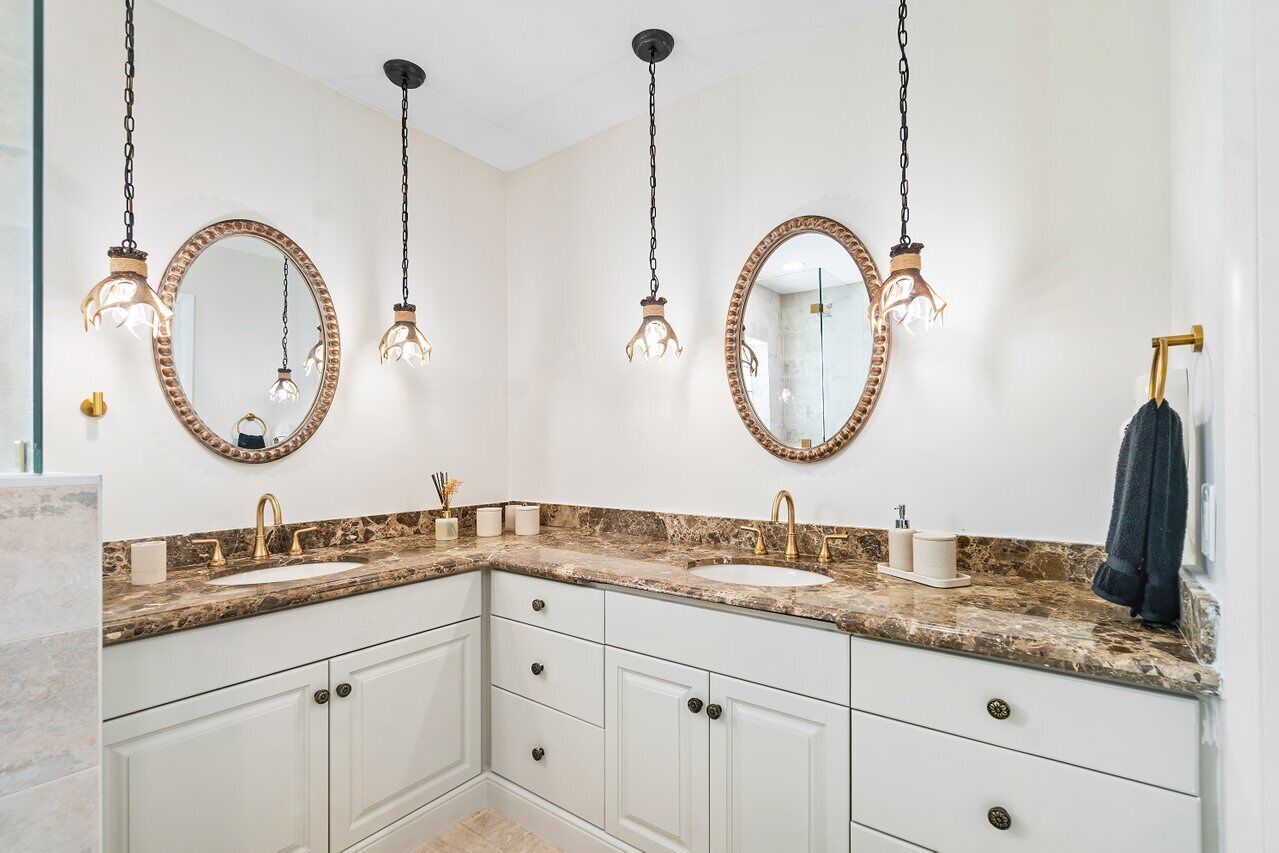 Un baño con dos lavamanos, muebles blancos y espejos decorativos con luminarias.