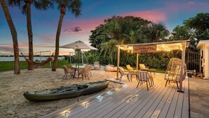 A beach club named 'The Garden of Eden' with outdoor seating, a hammock, and a kayak on the sand. - The Garden of Eden | Beautiful Villa w/ Pool & Game Room (West Palm Beach)