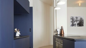 A modern kitchen with blue cabinetry, a central island, pendant lighting, and a framed picture on the wall.