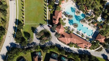 Surrounded by palm trees, this resort features a central pool, a green field, and a mix of modern and traditional architecture.