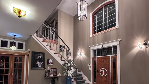 A spacious foyer with a black and white checkered floor, a wooden staircase, and a large vase with flowers.