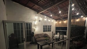 Een overdekte patio met een bank, eettafel, stoelen en potplanten.