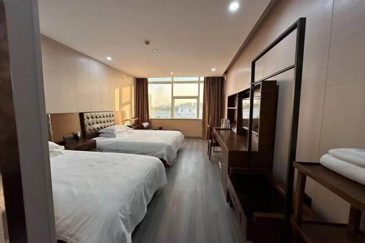A hotel room with two beds, a TV, a desk, and a window with a city view.