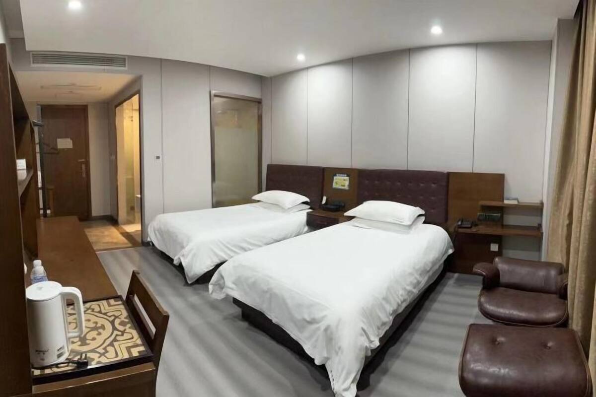 A hotel room with two beds, a coffee maker, a chair, and a desk.