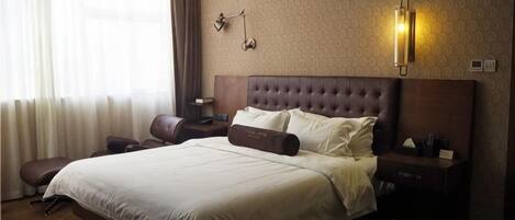 A hotel room with a large bed, a nightstand, a lamp, and a window with curtains.