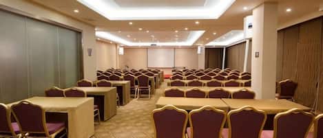 A conference room with rows of tables and chairs, a projector screen, and a carpeted floor.