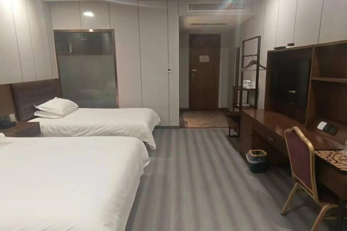 A hotel room with two beds, a desk, a chair, a TV, and a wardrobe.