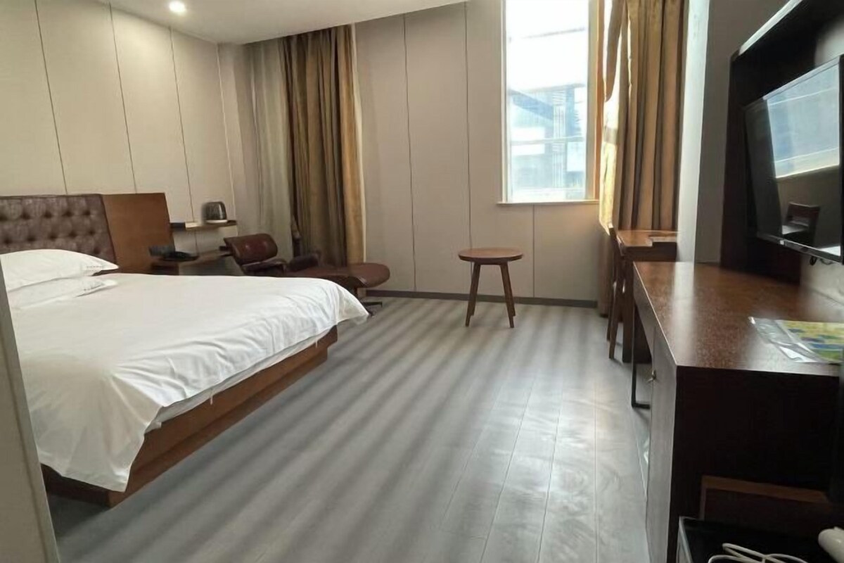 A hotel room with a bed, a desk, a chair, a small table, and a television.