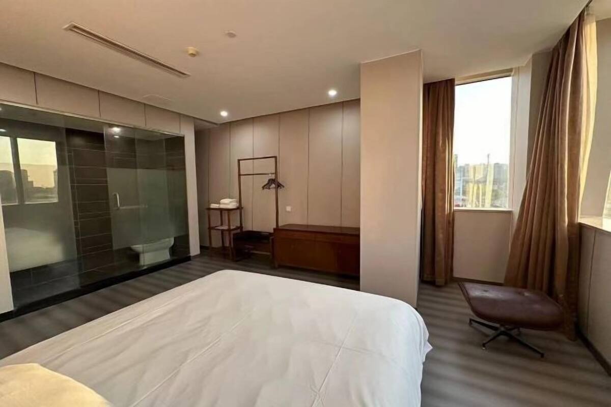A hotel room with a large bed, a seating area, a small table, a wardrobe, and a window with curtains.