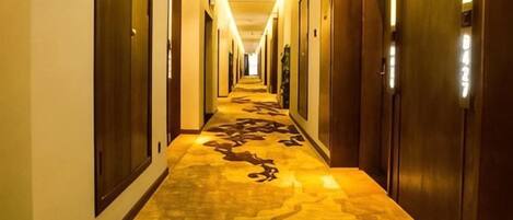 Un pasillo de hotel con puertas a ambos lados, una alfombra estampada y una lámpara en el techo.