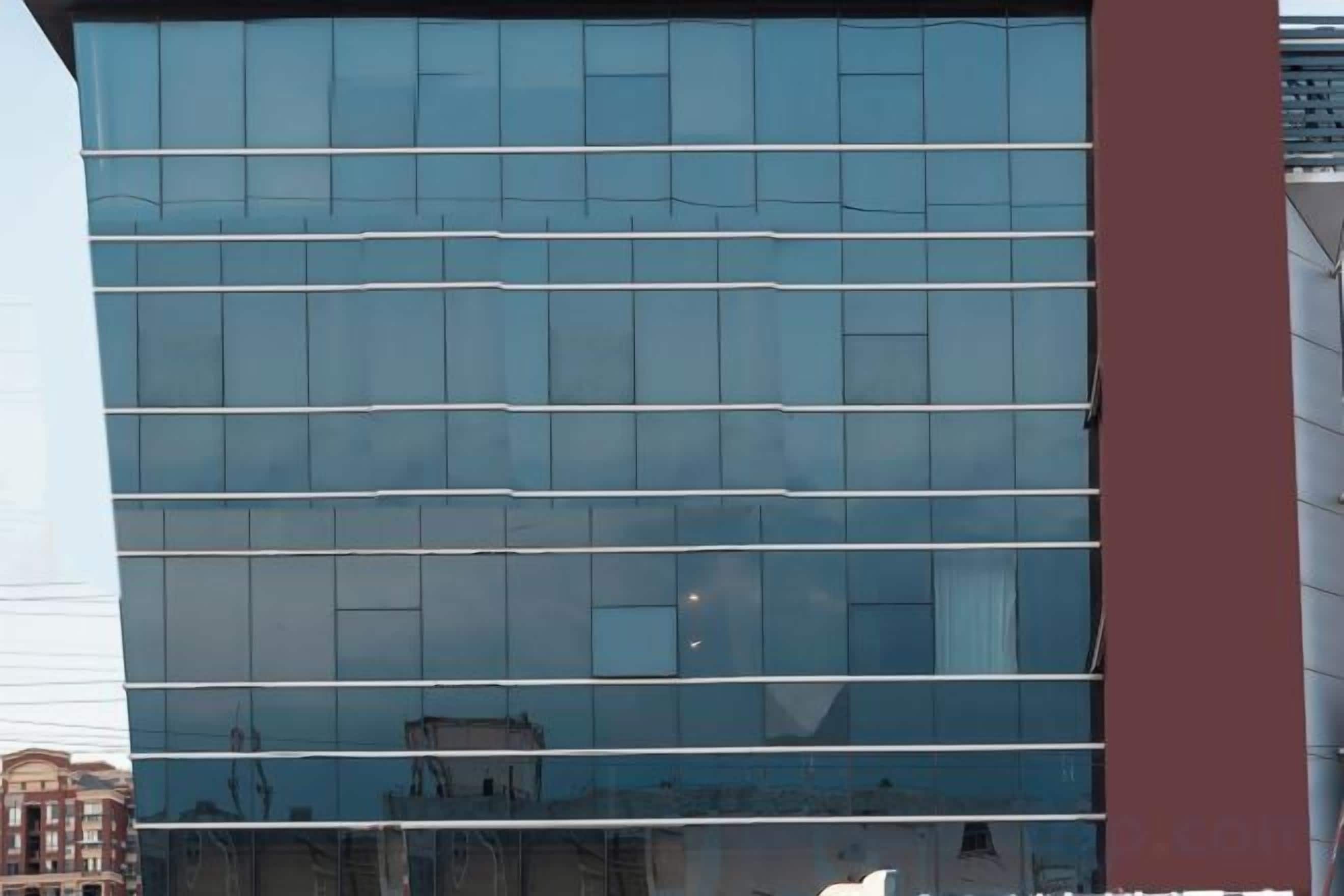 Un bâtiment moderne doté d’une façade en verre réfléchissant et d’un élément vertical rouge bien visible.