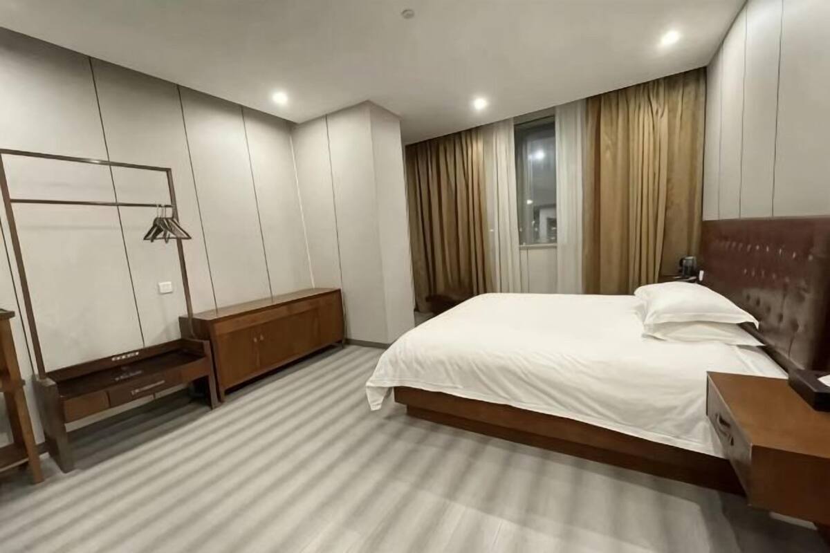 A hotel room with a large bed, a wooden dresser, a seating area, and a window with curtains.