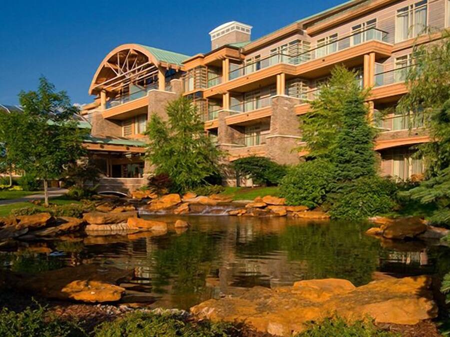 A multi-story hotel with a stone facade, a pond, and surrounding greenery.