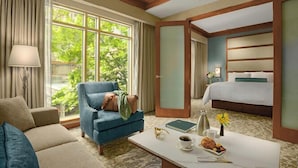 A hotel room with a blue armchair, a white coffee table with breakfast items, a bed with a white bedspread, and a view of greenery through large windows. - The Lodge at Turning Stone Resort Casino (Verona)