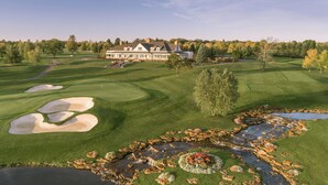 A golf course with bunkers, a pond, and a large house in the background. - The Lodge at Turning Stone Resort Casino (Verona)