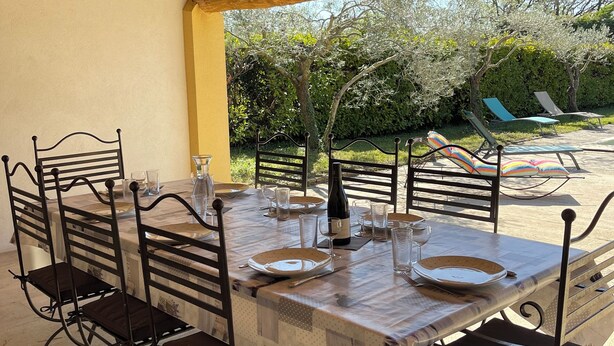 Ein Essbereich im Freien mit einer Holzw pergola, Metallstühlen und einem Tisch für sechs Personen.