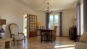 Ein geräumiges Wohnzimmer mit Essbereich, einer Chandelierleuchtre und Blick durch ein Fenster.