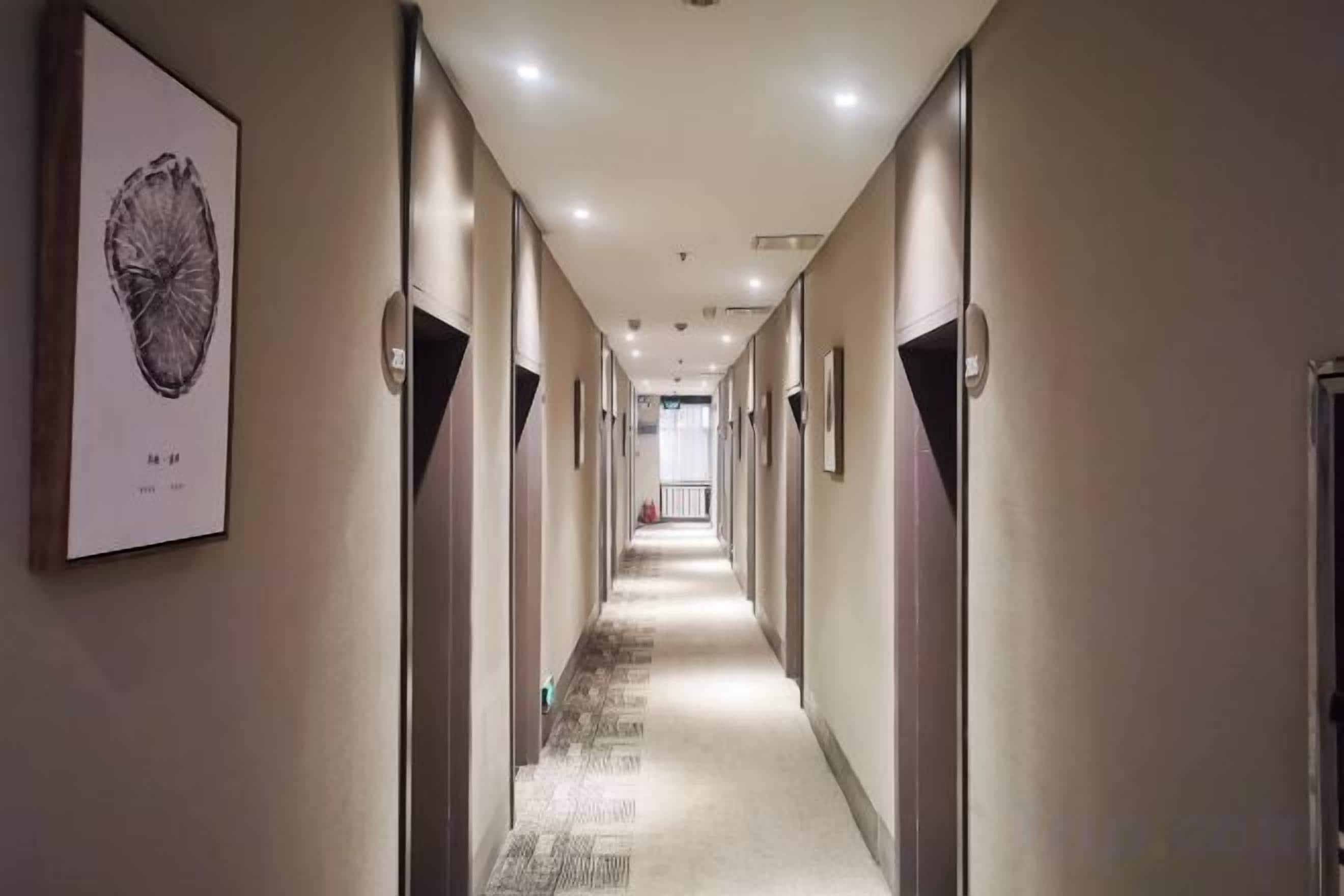 A hotel corridor with doors on both sides, a carpeted floor, and framed artwork on the walls.