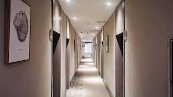 A hotel corridor with doors on both sides, a carpeted floor, and framed artwork on the walls.