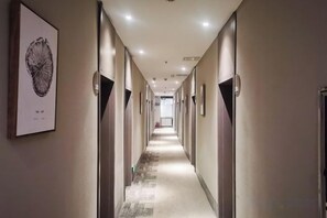 Een hotelgang met deuren aan beide kanten, een tapijtvloer en kunstwerken in lijsten aan de muren.
