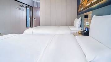 A hotel room with two beds, a small seating area, a nightstand, and a wall-mounted mirror.