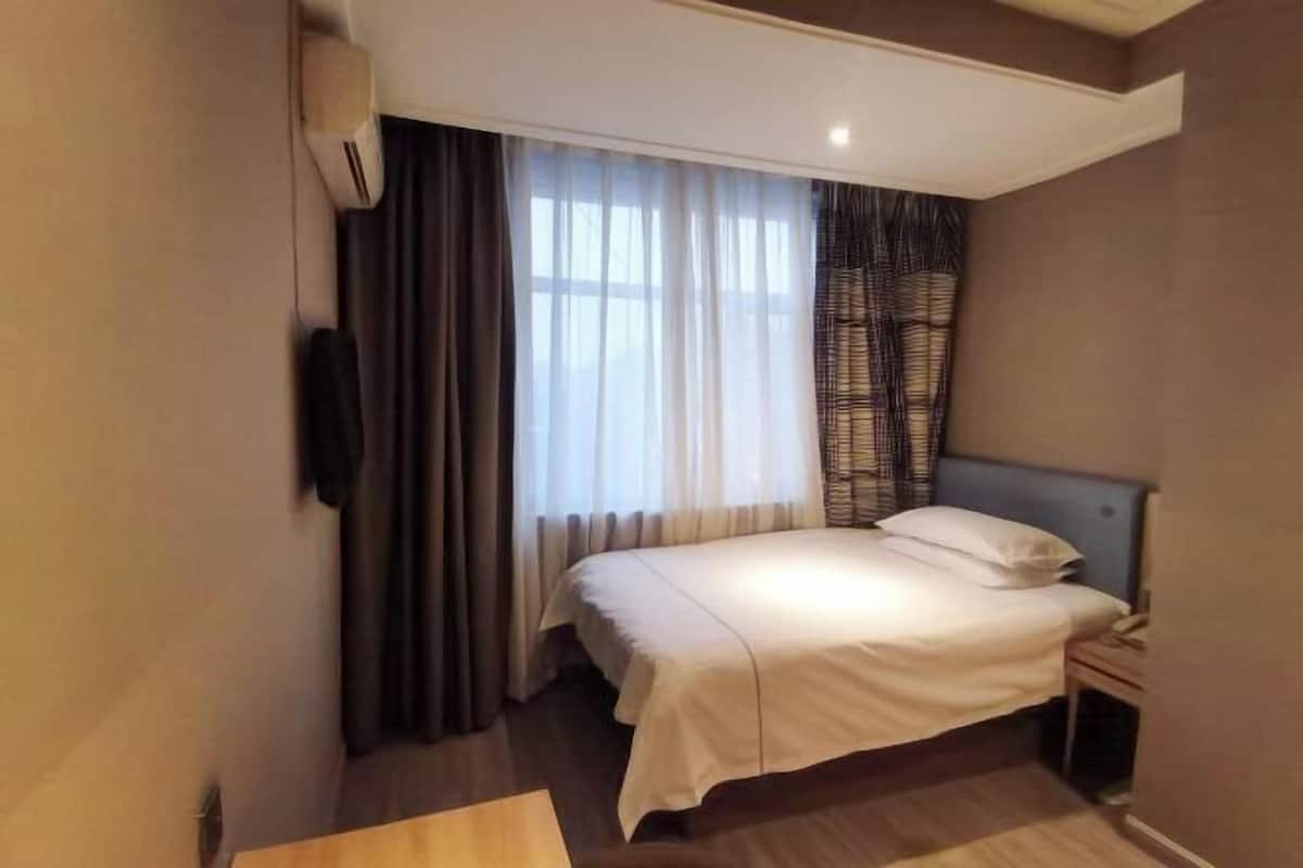 A hotel room with a bed, a bedside table, a TV, and a window with curtains.