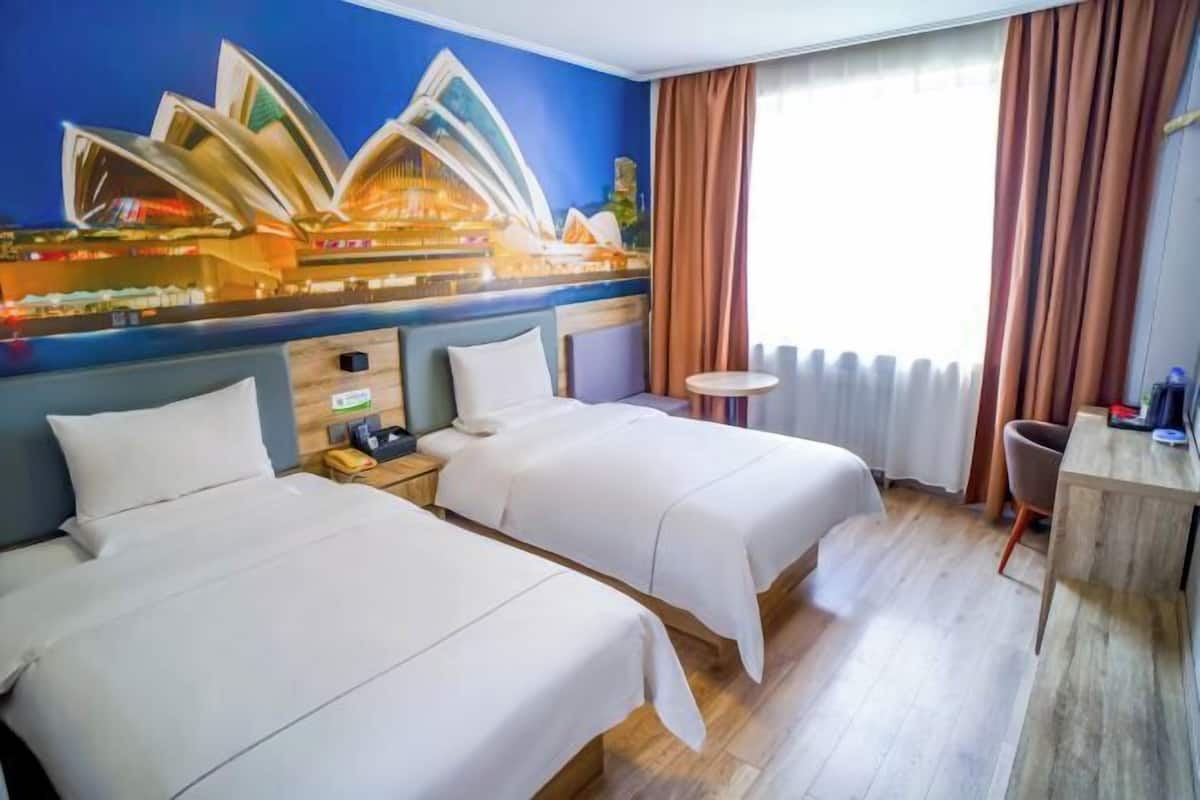 A hotel room with two beds, a small round table, a chair, a nightstand, and a wall mural of the Sydney Opera House.