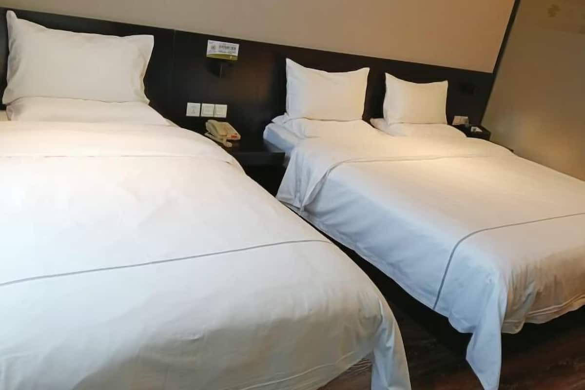 Two single beds with white linens, a bedside telephone, and a wall-mounted light switch.