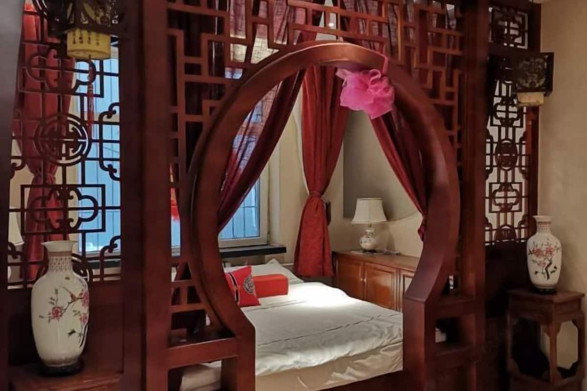 A traditional room with a bed, a window, a nightstand, and a decorative wooden screen.