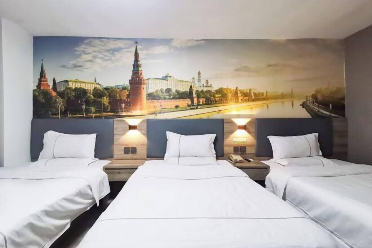 A hotel room with three beds, a large wall mural of a cityscape, and two bedside lamps.